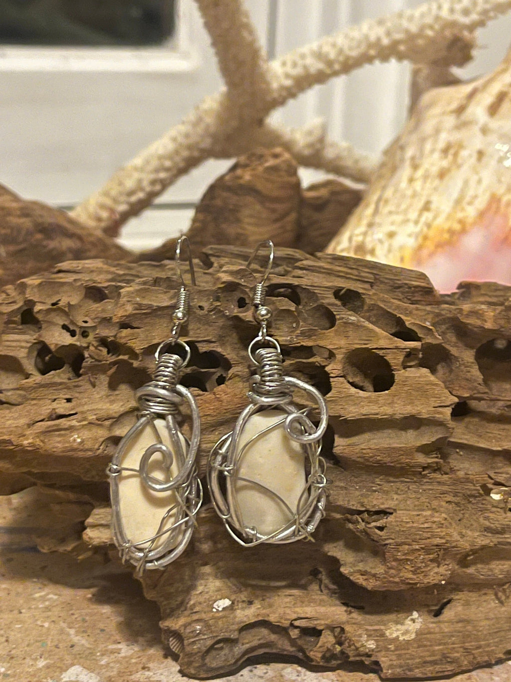 Silver wire-wrapped earrings with a shell fragment on a wooden surface.