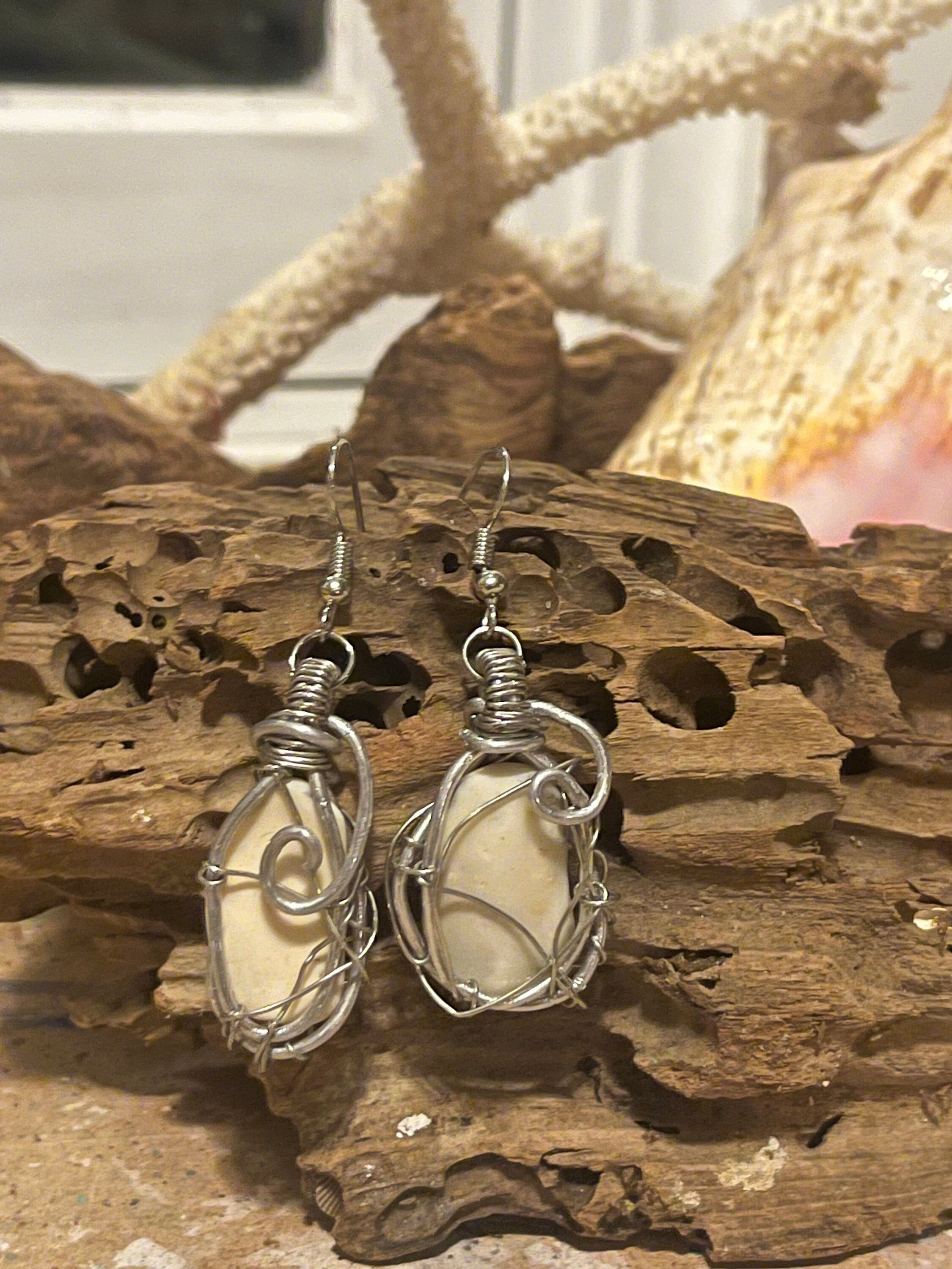 Silver wire-wrapped earrings with a shell fragment on a wooden surface.