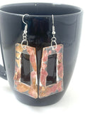 Rectangular earrings with floral design hanging in front of a black mug.