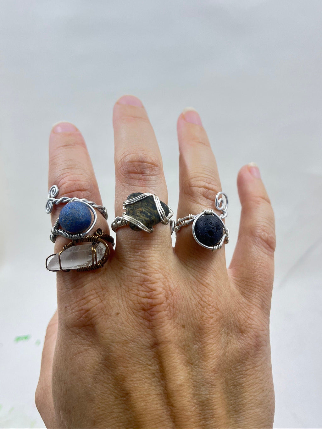 Hand wearing three silver rings with gemstones and one bronze ring on a white background