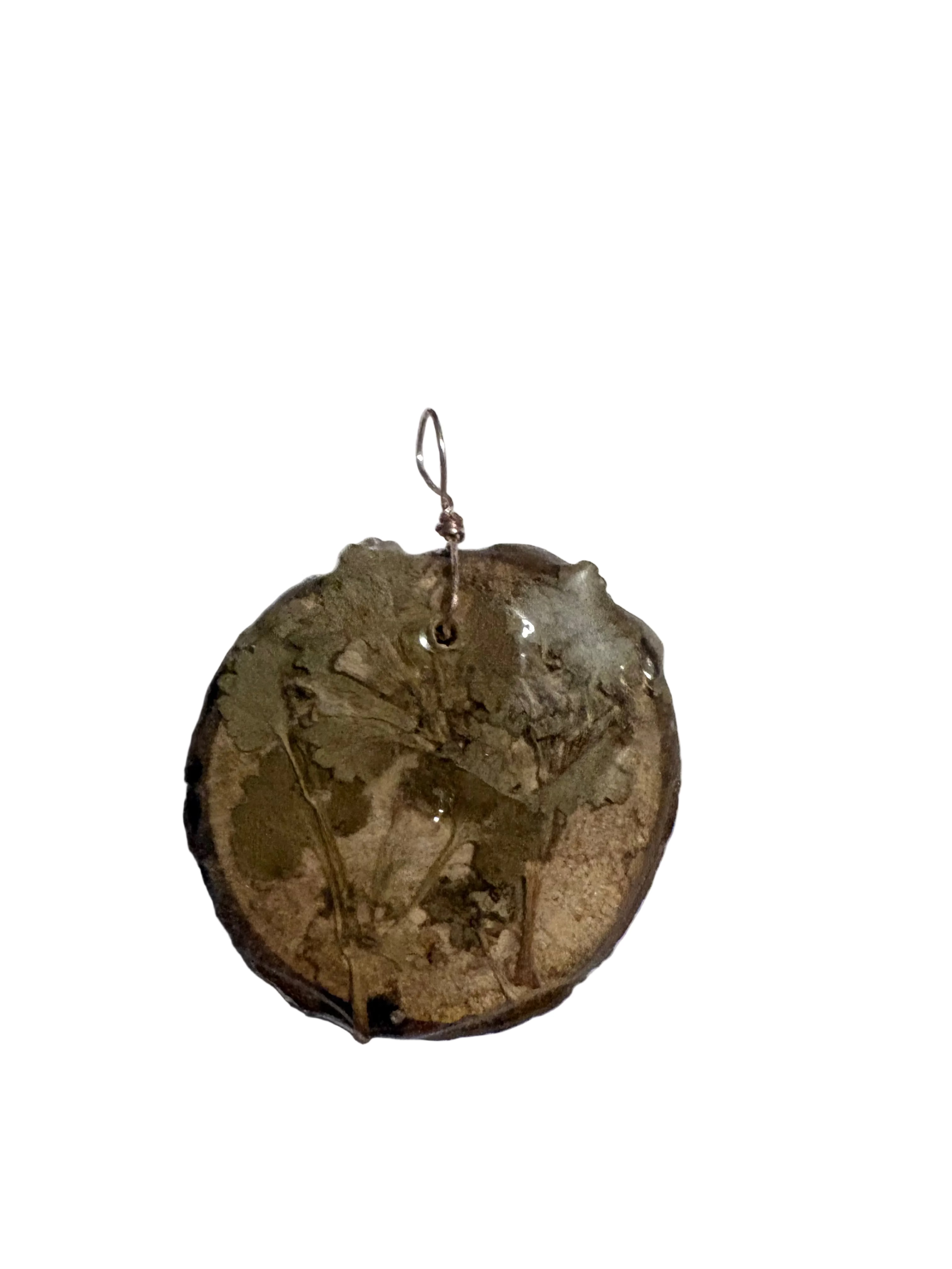A handmade circular wood pendant featuring a dried botanical specimen embedded in resin, suspended from a small metal loop on a plain light background.