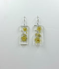 Rectangular clear earrings with pressed flowers on a light gray background