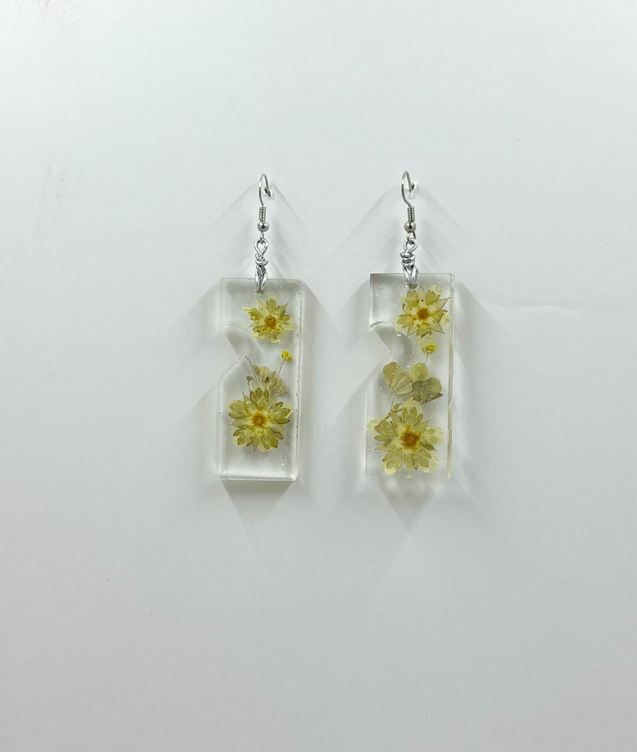 Rectangular clear earrings with pressed flowers on a light gray background