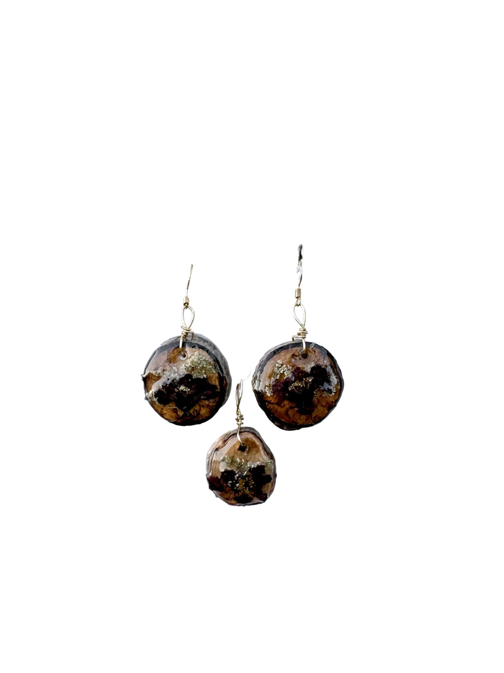 Three wood slice pendants in earthy brown, with burgandy flowers, suspended from gold wire hooks on a white background.