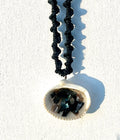 Necklace with a shell pendant featuring black and blue stones on a white background