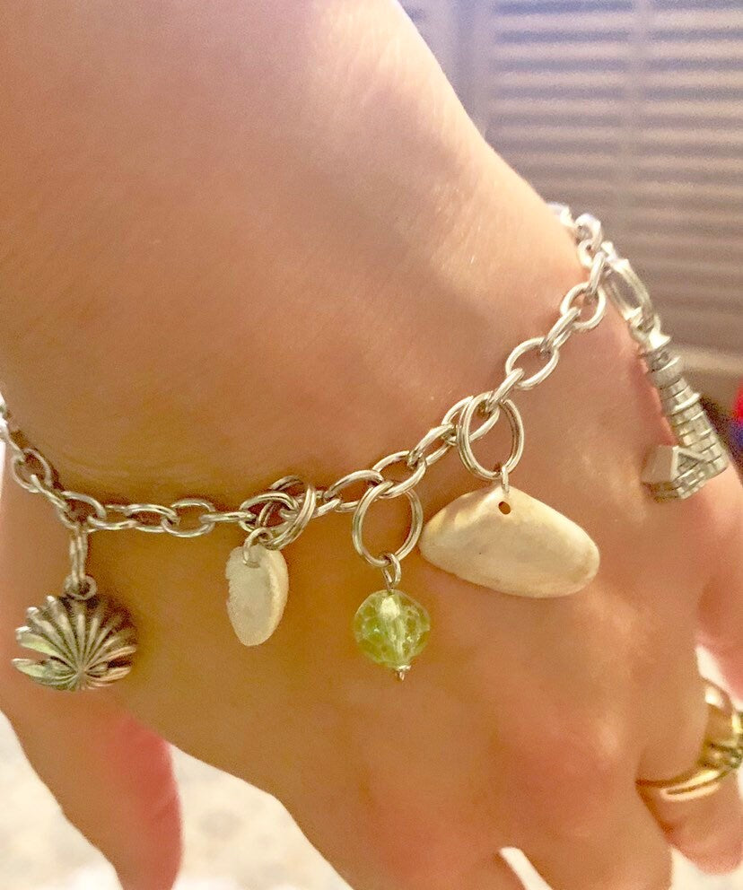 Silver bracelet with shell,  and bead charms on a hand against a blurred background