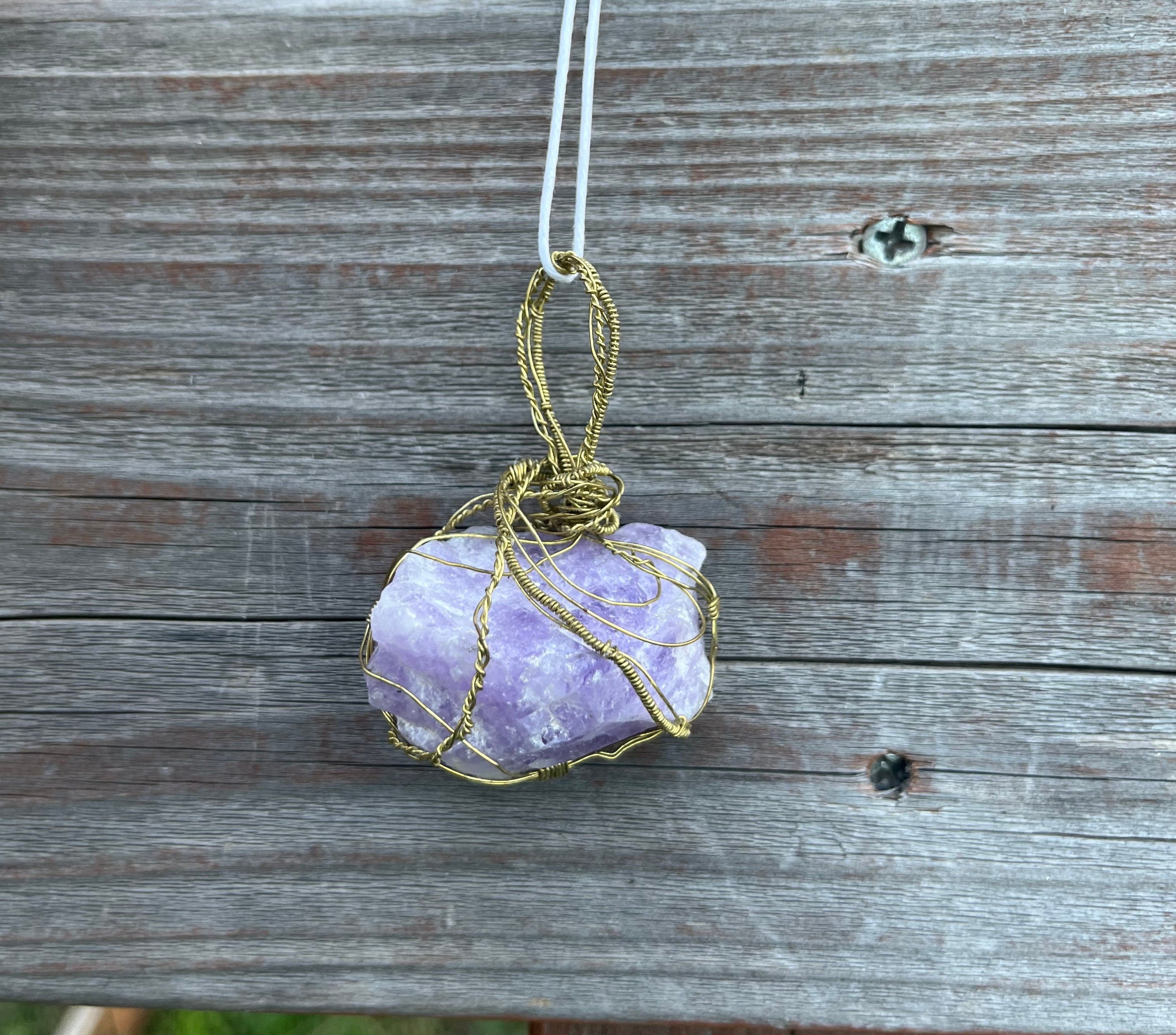 Purple crystal pendant with gold wire wrapping on a wooden surface