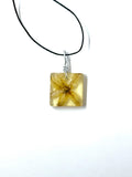 Square pendant with floral design on a black cord against a white background