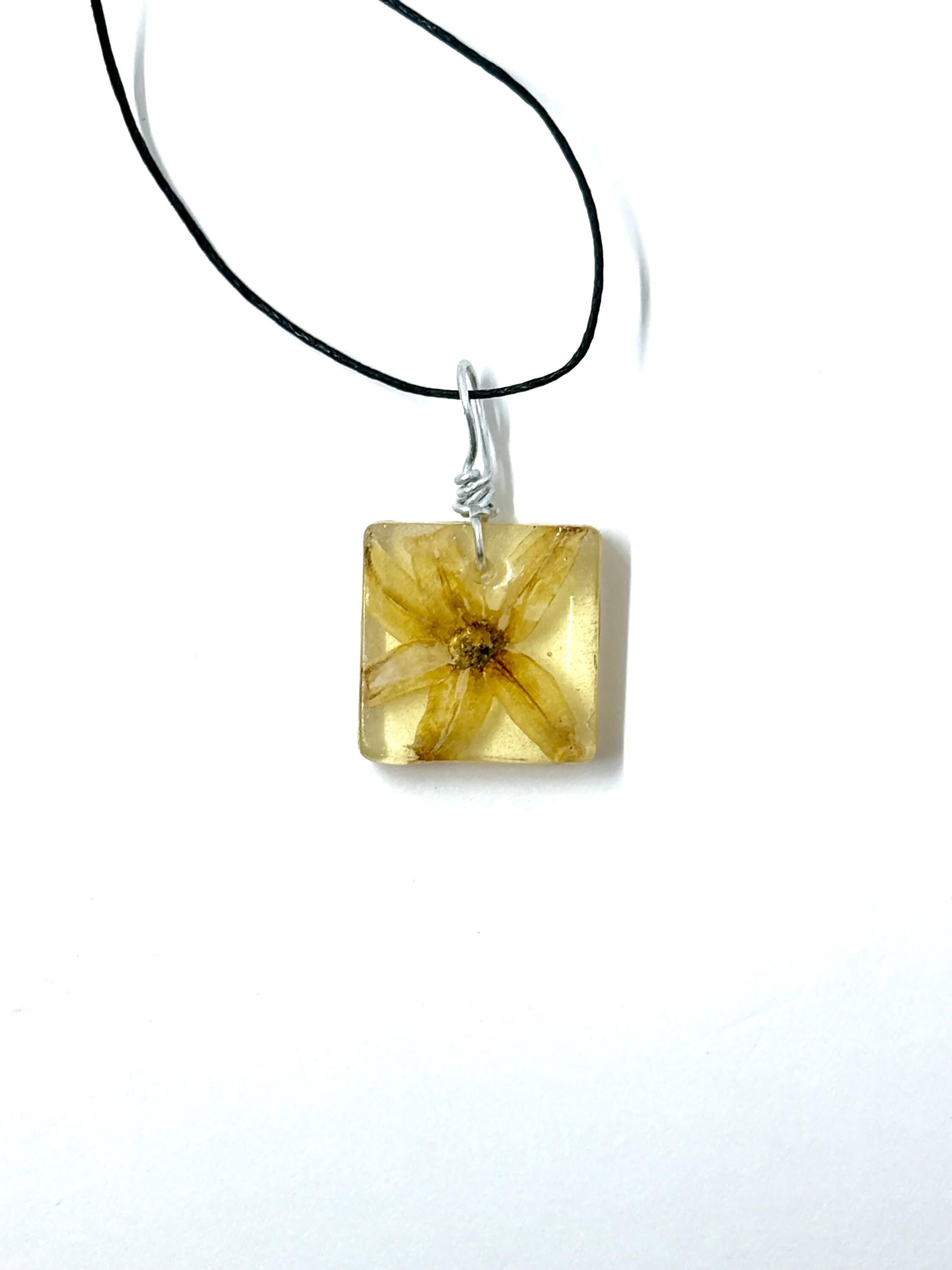 Square pendant with floral design on a black cord against a white background