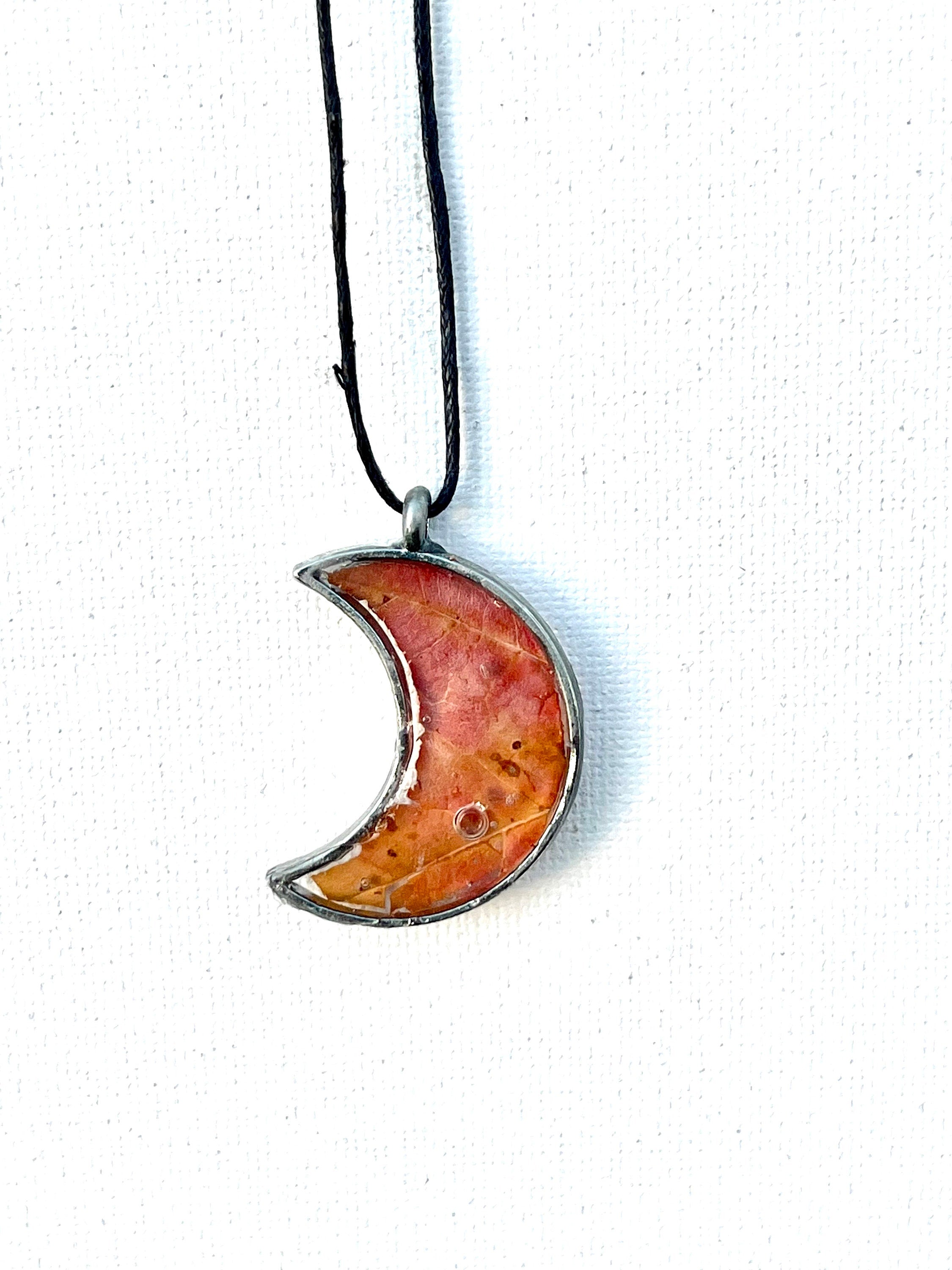 Crescent moon-shaped pendant on a black cord against a white background
