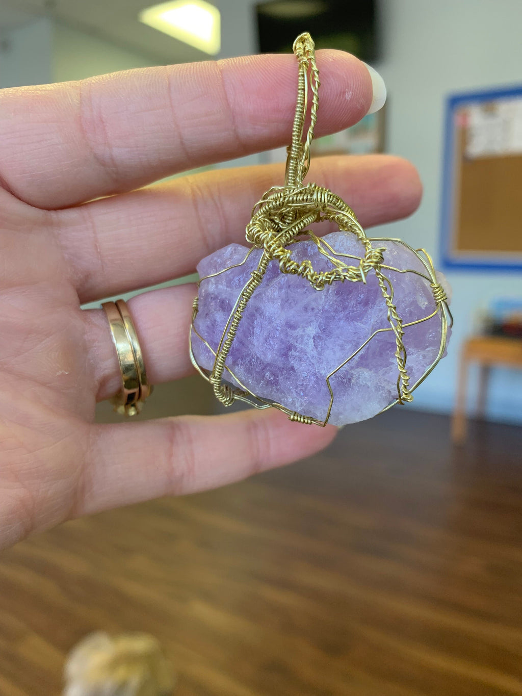 Hand holding a purple stone pendant with gold wire wrapping in an indoor setting