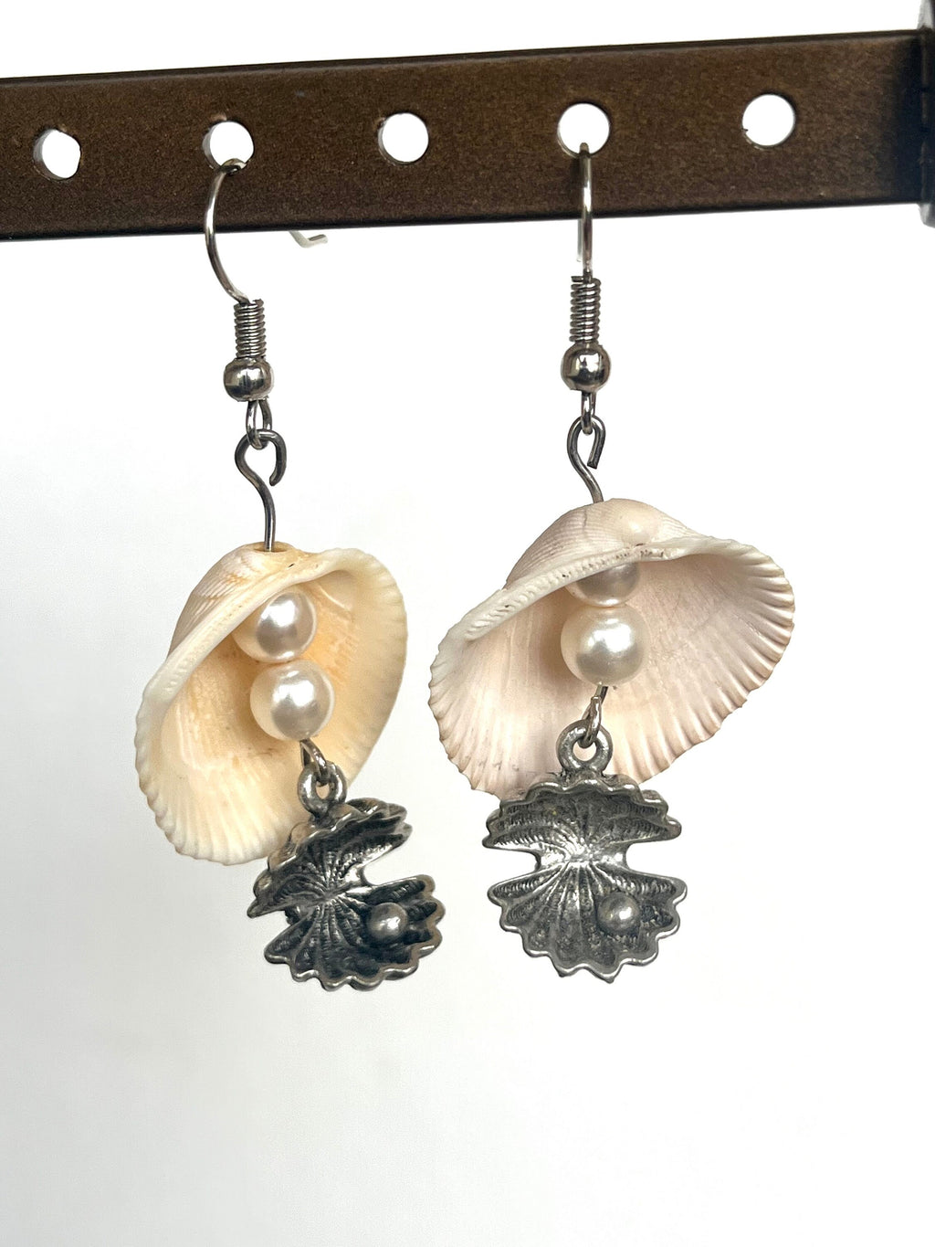 Shell and pearl earrings hanging on a hook against a white background