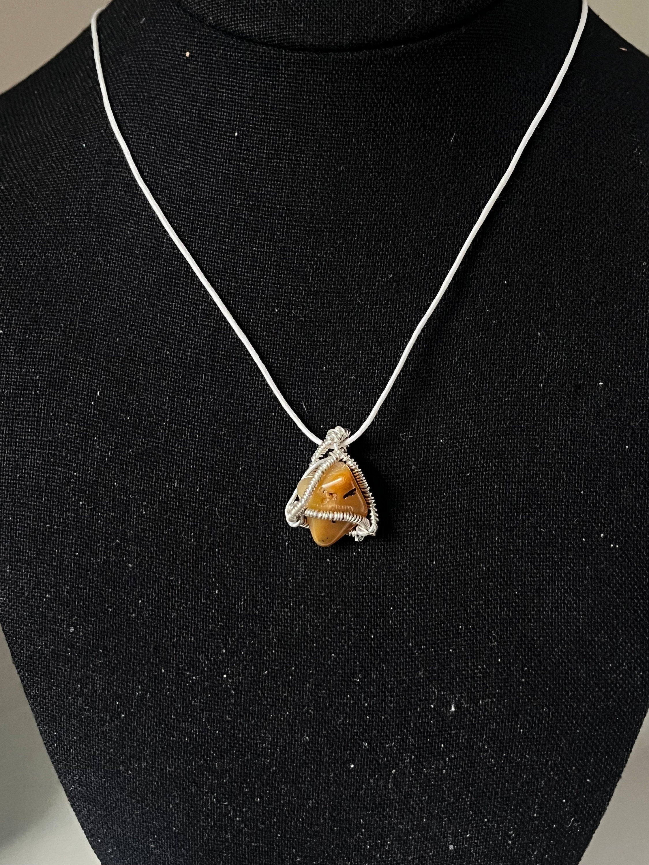 Necklace with a pendant featuring a yellow stone on a black stand.