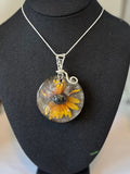 Round pendant with a sunflower design on a black mannequin bust.