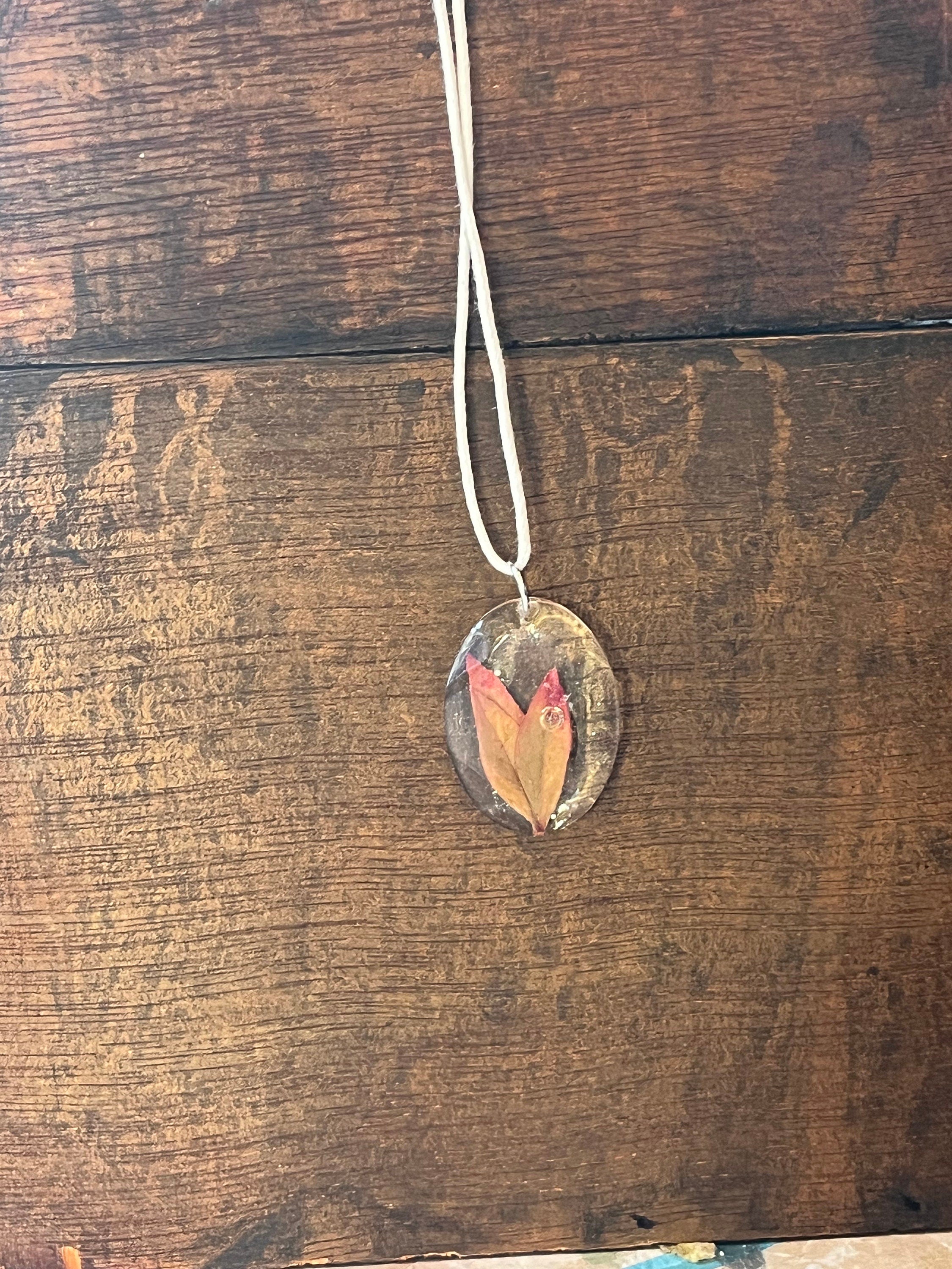 Necklace with a pendant featuring leaves on a wooden surface