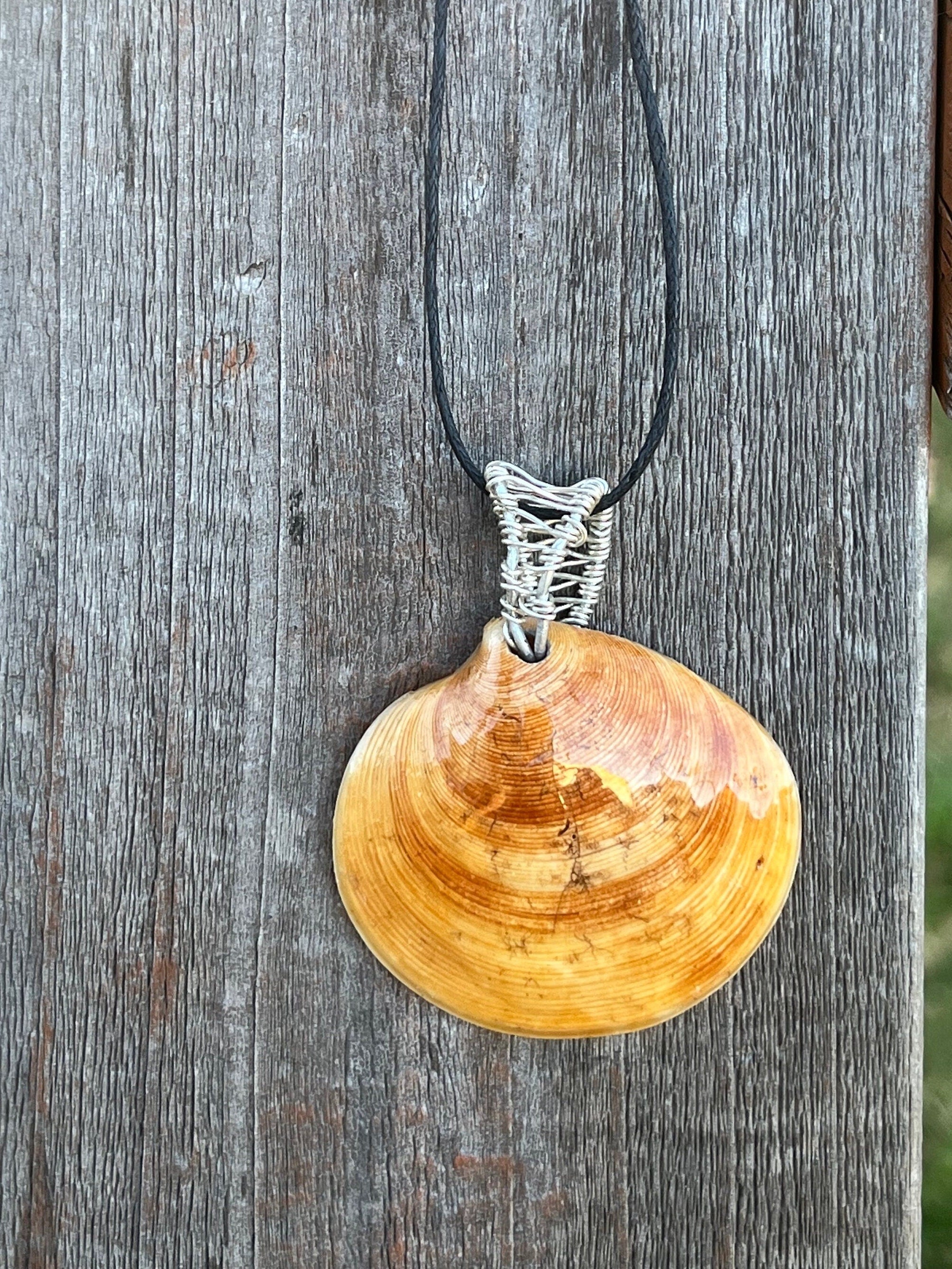 Shell pendant with silver wire wrapping on a black cord against a wooden background
